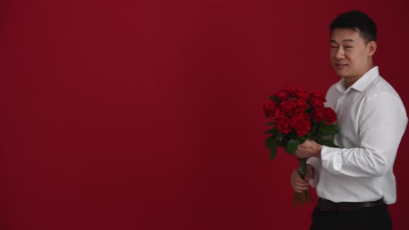 Smiling Asian man holding a bouquet of red roses and walking