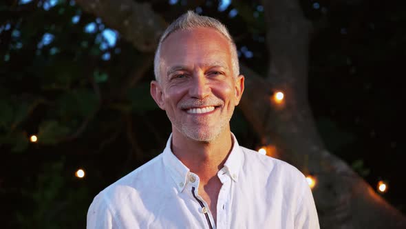 Close Up Ortrait of Happy Mature Man with Gray Hair Looking and Smiling at Camera Outdoor at Sunset