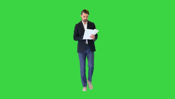 Serious Young Businessman Reading Documents While Walking on a Green Screen Chroma Key