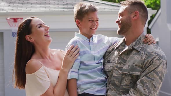 Happy caucasian male soldier embracing his smiling son with wife in garden outside their house