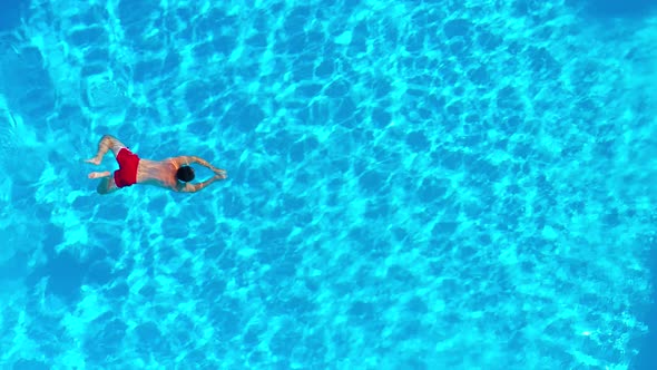 Aerial View of a Man in Red Shorts Swimming in the Pool