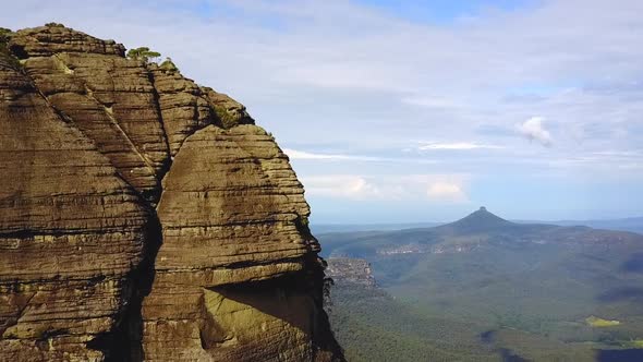 Drone circling cliff face revealing mountains and rocky escarpments in the background. Location NSW,