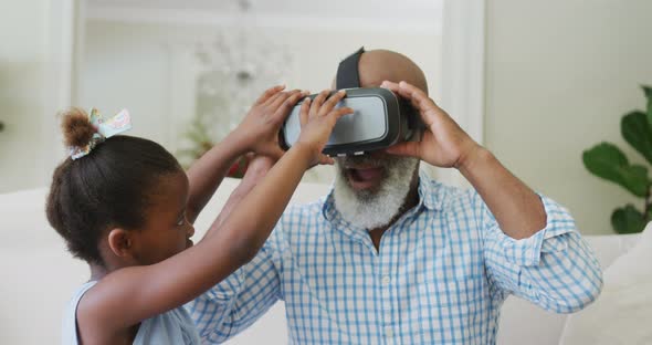 Happy african american grandfather using vr headset with granddaughter in living room