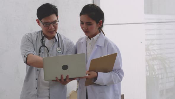 Doctor hold laptop and discuss with coworker in room with glass window