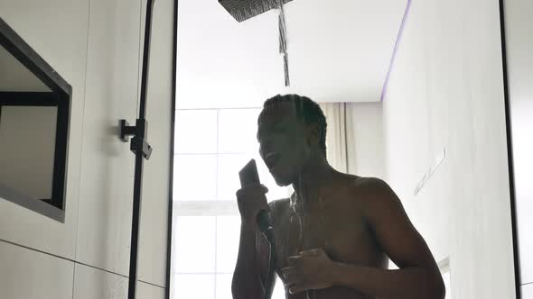 Happy African American Man Takes a Shower and Sings Songs in Front of a Bright Window