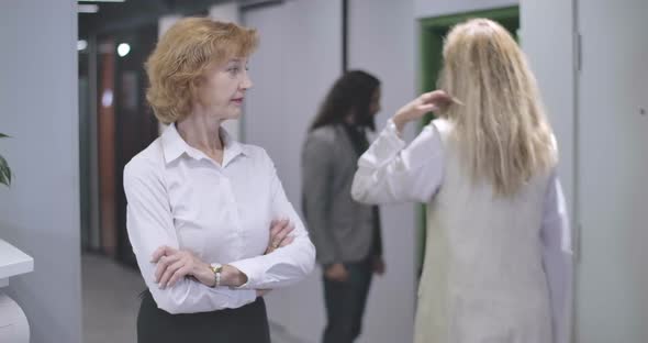 Portrait of Serious Middle Aged Caucasian Woman Standing with Hands Crossed in Open Space Office