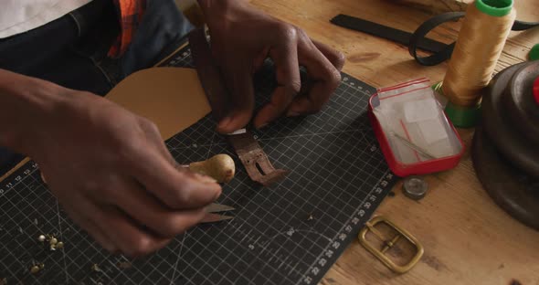 Hands of african american craftsman preparing belt in leather workshop