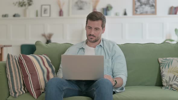 Young Man with Laptop Celebrating Success on Sofa