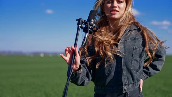 Beautiful woman singing with microphone in green field