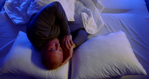 Close-up Portrait of a Bald, Middle-aged Man Lying in Bed with White Linens and Two Pillows. He's