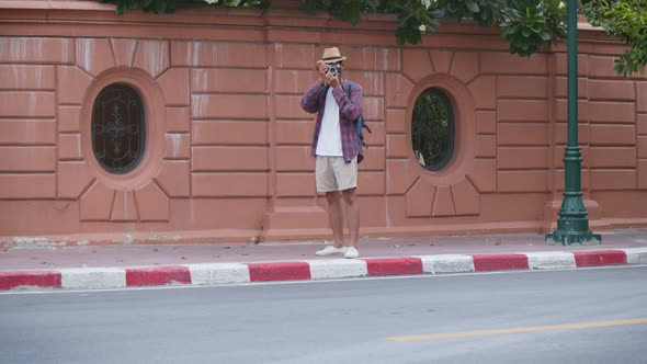 Tourist Asian man uses a camera to take a photo while standing beside the street in Thailand.