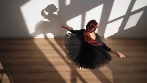 Ballerina in Black Tutu Gracefully Dances Against White Wall in Bright Sunlight