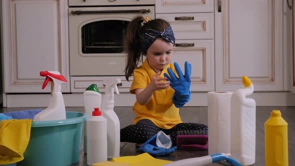 Closeup of a Little Girl Wearing Rubber Gloves Sitting at Home on the Floor