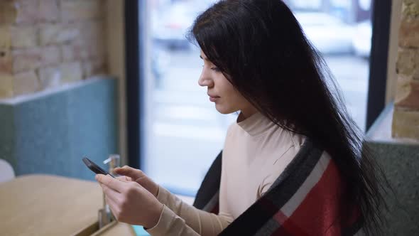 Side View Happy Relaxed Middle Eastern Woman Surfing Social Media on Smartphone Sitting in Cafe