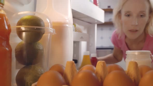 Mature Woman Taking Bottle of Cream Sauce From Fridge