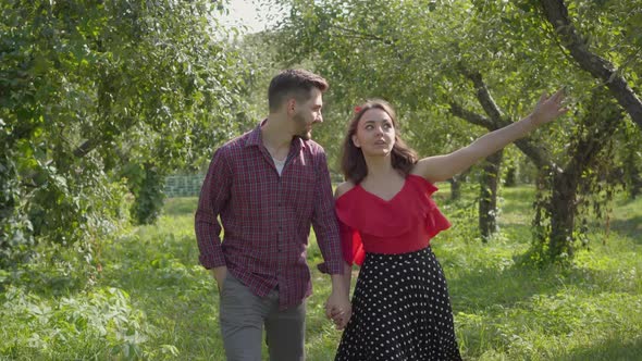 Young Couple in Love Walking Through the Garden Holding Hands and Talking