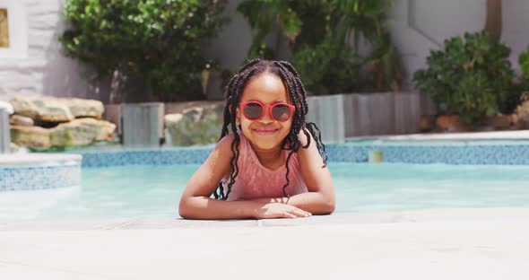 African american girl wearing sunglasses in swimming pool smiling at camera