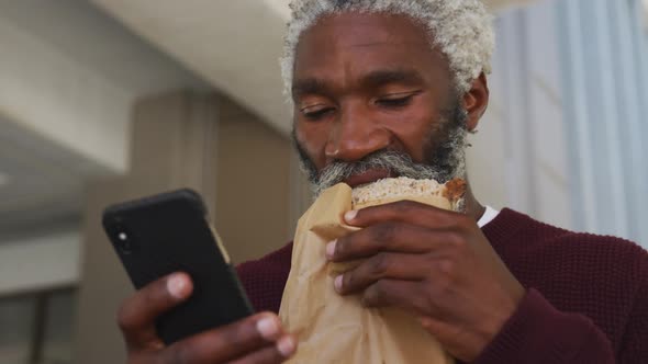 African american senior man having a snack and using smartphone at corporate park