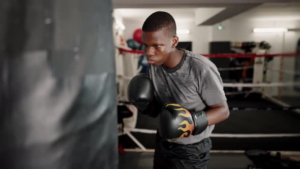 Young Concentrated African Male Boxer Hitting Punching Bag in Boxing Club