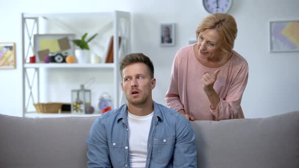 Nervous Mother Talking to Adult Son Sitting on Sofa at Home, Family Conflict