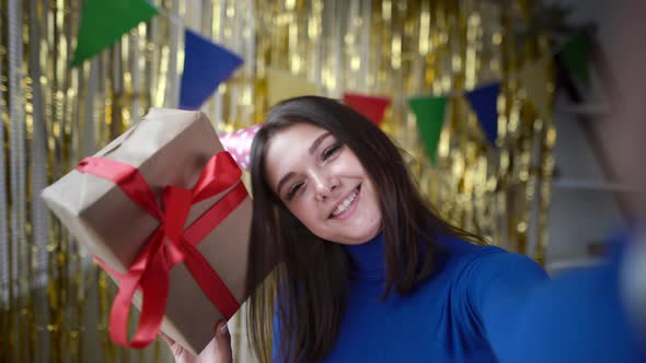 Happy Caucasian Millennial Girl Shows a Box with a Gift at Her Birthday on a Smartphone Camera