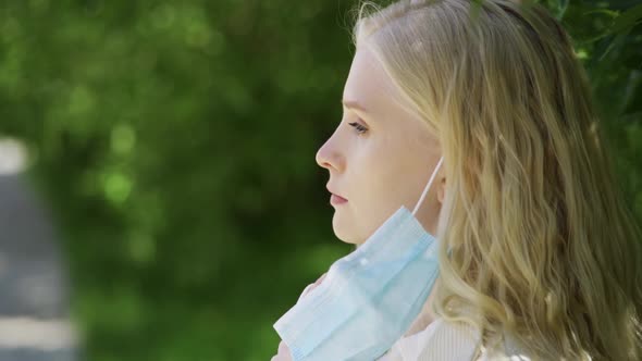 Young Woman Enjoys the Smell of a Yellow Dandelion Without a Medical Mask in the Park