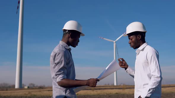 Two Male African American Electrical Engineers Stand Against the Backdrop of a Windmill at an Air