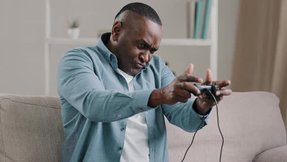 Focused Mature African American Man Sitting in Room on Couch Holding Controller Playing Computer