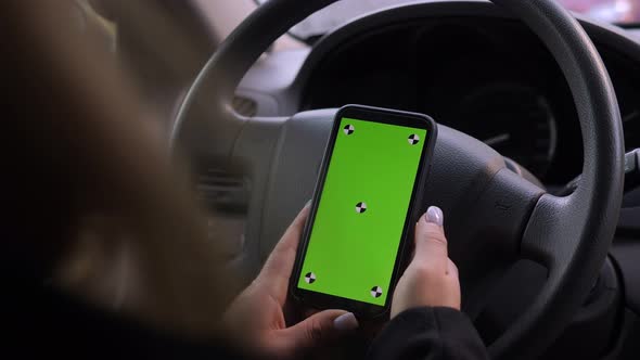 Closeup of a Woman Holding a Phone with a Green Screen While Driving a Car