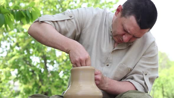 Male Makes a Clay Jug on a Rotating Circular Loom Outdoors on a Sunny Bright Day