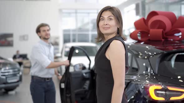 Young Slim Woman Looking at Man Opening Car Door at the Background, Turning To Camera and Dancing