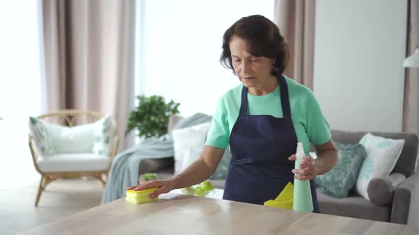 Elderly American Woman Housekeeper Wipe Table Working in Home Room