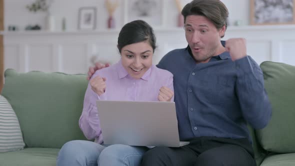 Man Hugging Indian Woman while using Laptop on Sofa