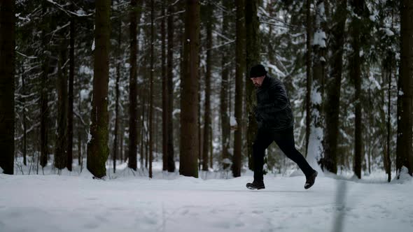 Adult Man in Black Clothes is Running in Snowy Forest in Winter Day Training and Sporty Activity