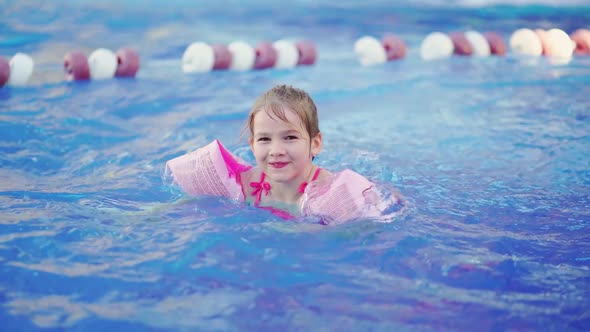 a Funny Little Girl Swims in Inflatable Armbands in a Pool