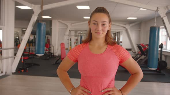 Portrait of a Young Smiling Girl in a Pink Tshirt Who Stands in the Middle of the Gym with Her Hands