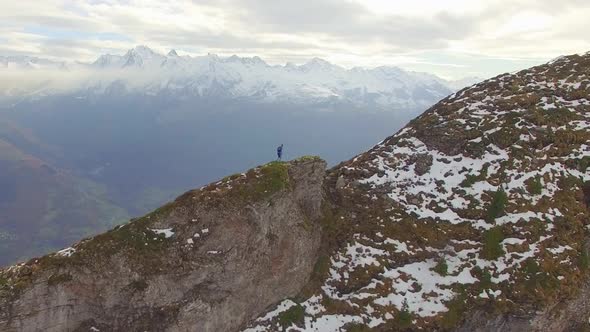 Aerial view of a trail runner running up the ridge of a snowy mountain