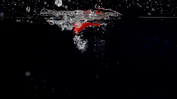 Vibrant red sweet pepper being dropped into water in slow motion.