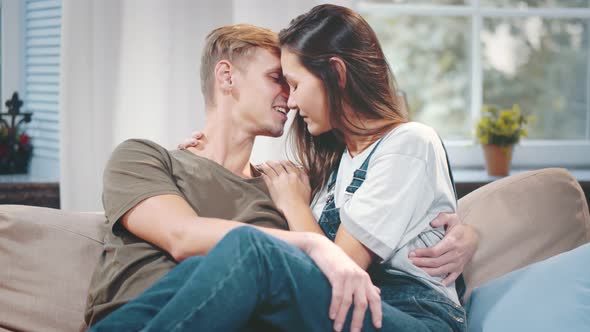 Beautiful Young Couple Talking and Cuddling Relaxing on Couch in Living Room