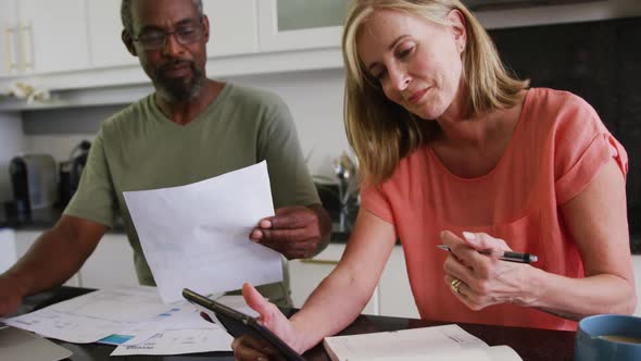 Diverse senior couple using tablet computer paying bills in kitchen