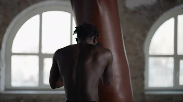 Shirtless Male Boxer Training at Boxing Studio with Wrapped Hands Rear View