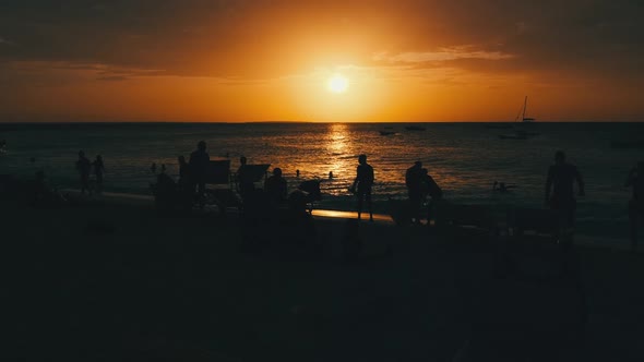 Silhouettes of People at Sunset Having a Rest By Ocean on the Beach Zanzibar