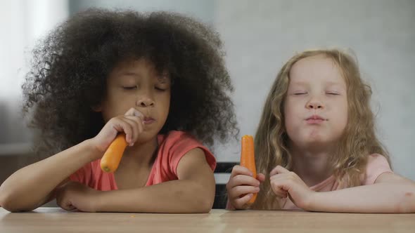 Two Pretty Little Girls Sitting at The Table and Eating Carrot with Appetite