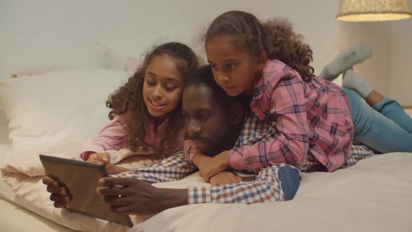 African Father with Kids Sharing Tablet Pc on Bed