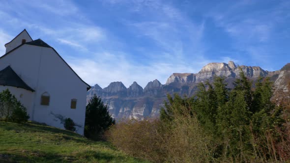 Panning shot from a mountain panorama to a ancient small chapel while fall in Switzerland.