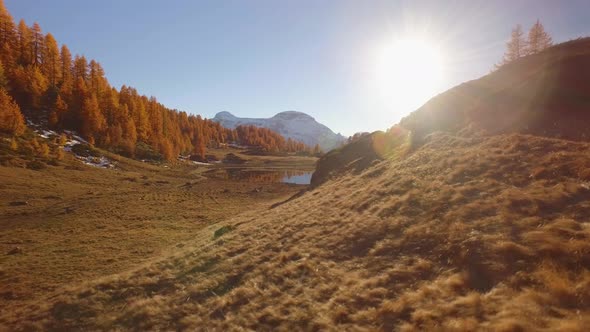 Side POV Walking on Fall Field Path Near Lake with Sun and Snowy Mounts