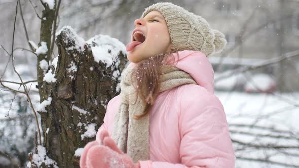 A Girl Playing with Snow in Winter Eating Snow with Tongue and Closed Eyes Outdoors in Winter