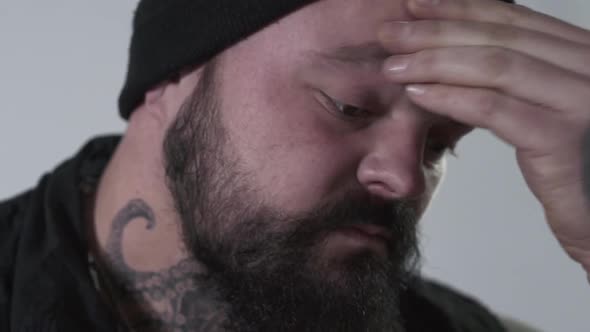 Aggressive Bearded Man Rubbing His Forehead To Hold Back Emotions. The Brutal Guy with Tattoos on