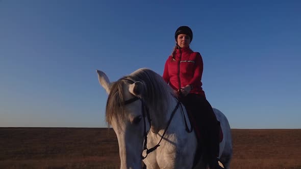 Girl Sitting on a Horse Looks Into the Distance in the Field Against a Sky