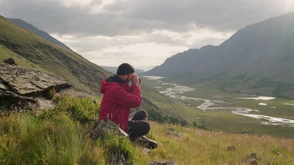 A young adventure photographer takes pictures around. Sitting on a mountain, against the backdrop